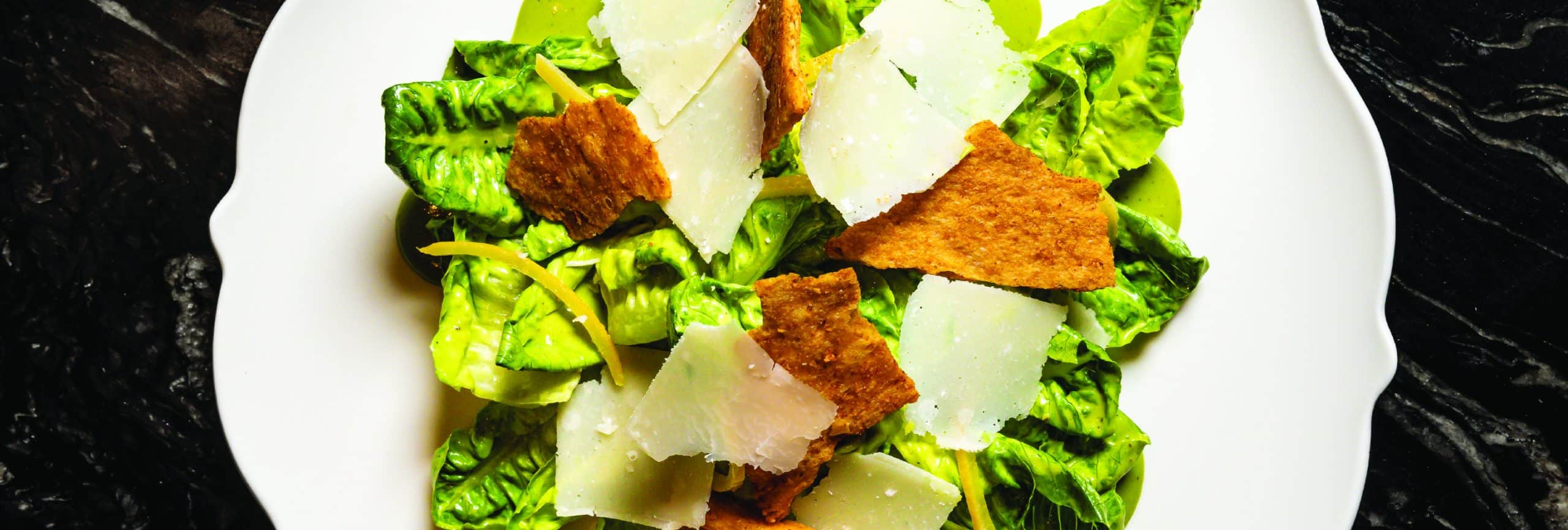 A fresh salad featuring croutons and crisp lettuce served on a white plate, showcasing vibrant colors and textures.