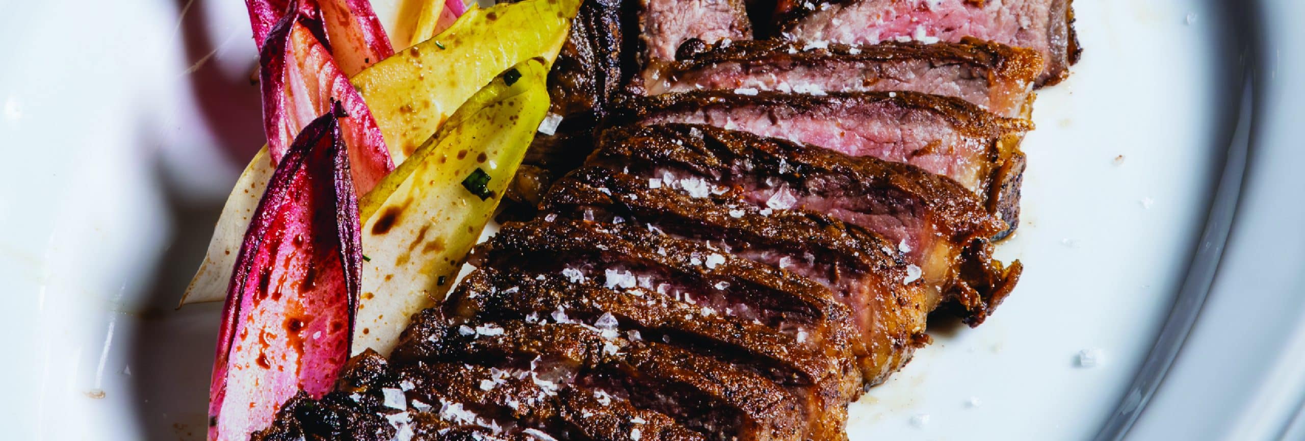 A beautifully plated steak accompanied by a variety of colorful vegetables on a pristine white plate.